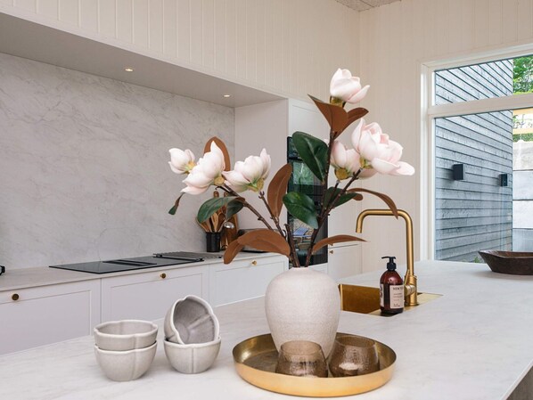 Een moderne keuken met een marmeren aanrechtblad, een vaas met bloemen en een gouden dienblad met glazen.