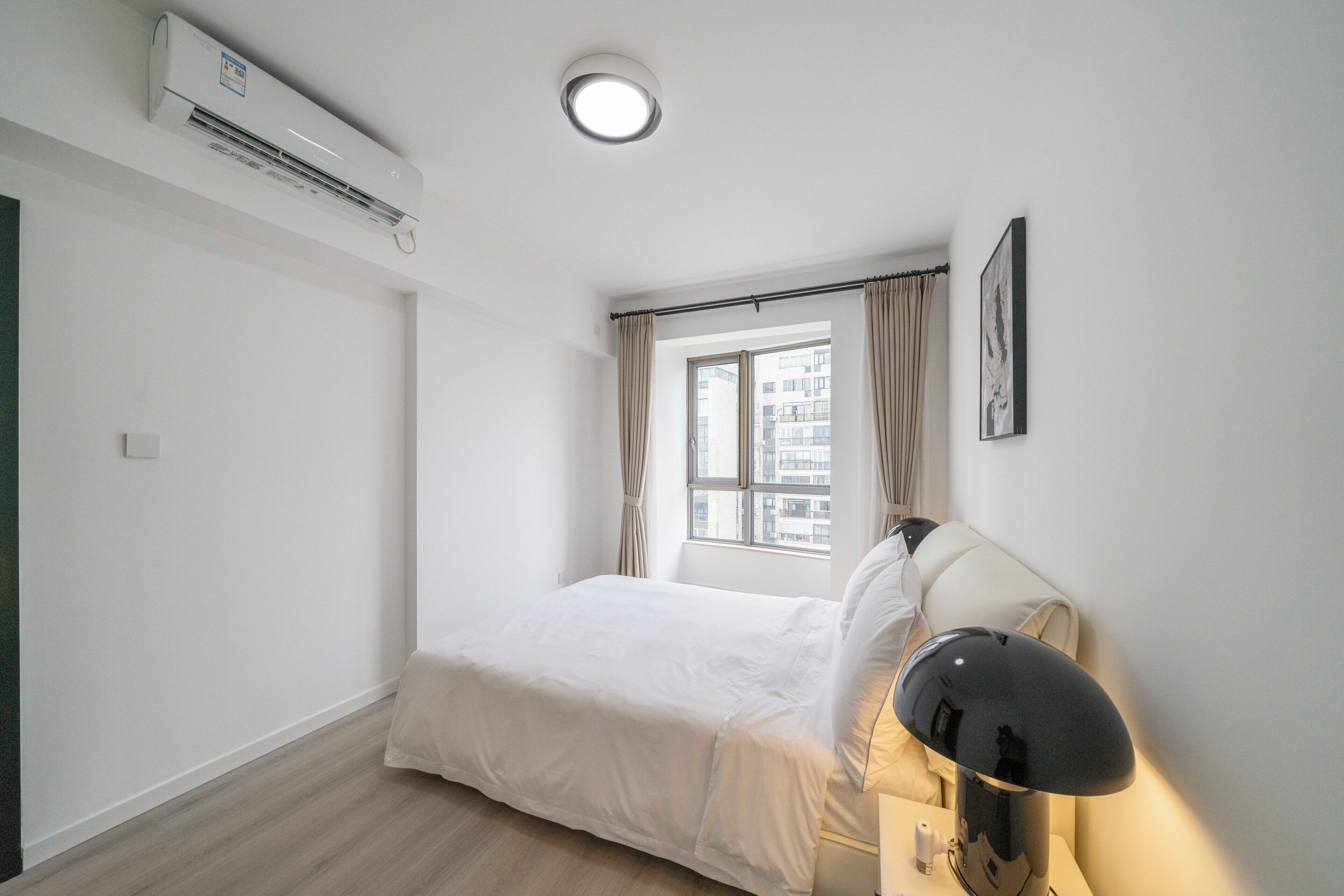 A minimalist bedroom with a bed, a bedside lamp, and a window with curtains.