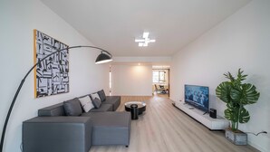 A modern living room with a grey sectional sofa, a flat-screen TV, a floor lamp, and a large plant. - Tyms Spacious 3BR 2BA APT  Laishi Di (Shanghai)