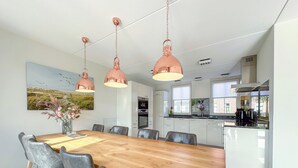 Une cuisine moderne avec des meubles blancs, une table à manger en bois et un luminaire suspendu en cuivre.