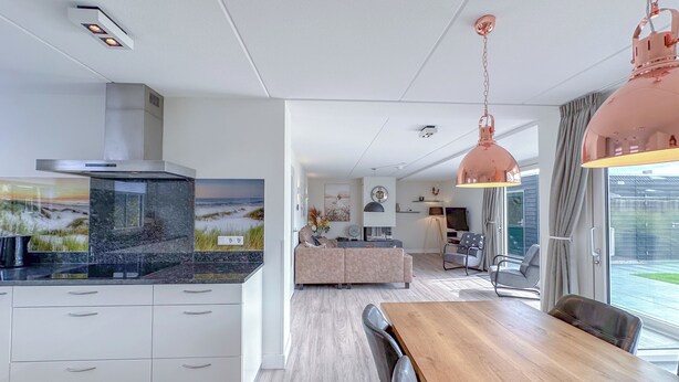 Une cuisine moderne dotée d’un grand îlot central, un coin repas avec une table en bois et un espace de vie comprenant un canapé et un téléviseur.