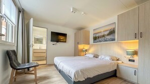 Une chambre à coucher moderne avec un lit, une chaise, un téléviseur et un tableau accroché au mur.