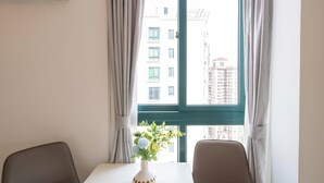 A room with a table, two chairs, a window with curtains, and a vase with flowers. - Tyms Yadu Business 1BR APT   (Shanghai)