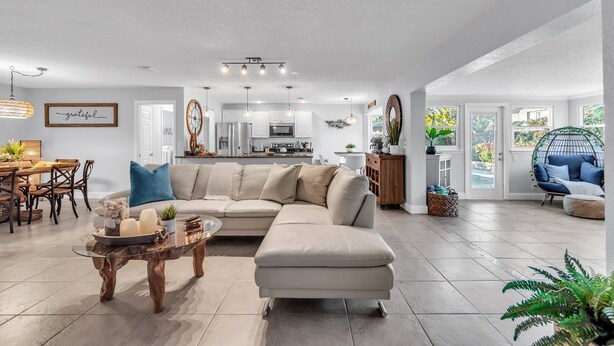 A spacious living area with a large beige sectional sofa, a glass coffee table, and a dining area with a wooden table and chairs. - Updated! Heated Pool! Near Beach! Grill, Parking, Outdoor Oasis! ~ Rosemary's Hacienda (Largo)