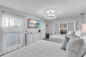 A bedroom with two beds, a dresser, a TV, and a ceiling light.