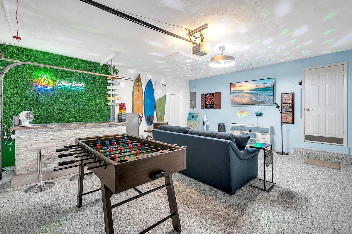A room with a foosball table, a sofa, a TV, and a neon sign.