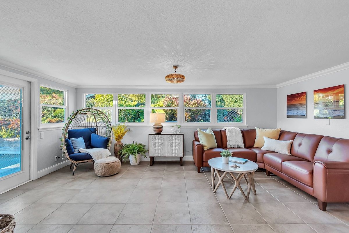 A sunlit room with a large window, a hanging chair, a sofa, and a coffee table.