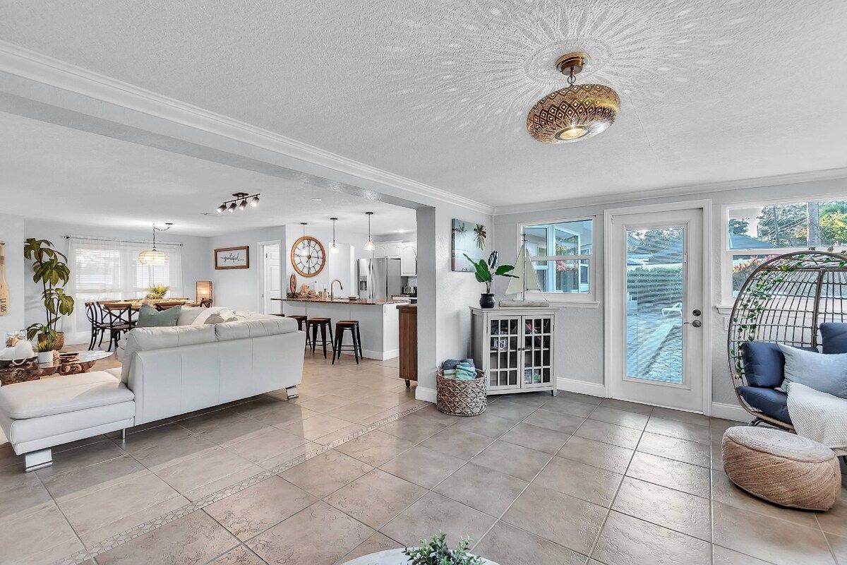 A spacious living area with a sofa, dining table, and chairs, a kitchen in the background, and a large window with a view.