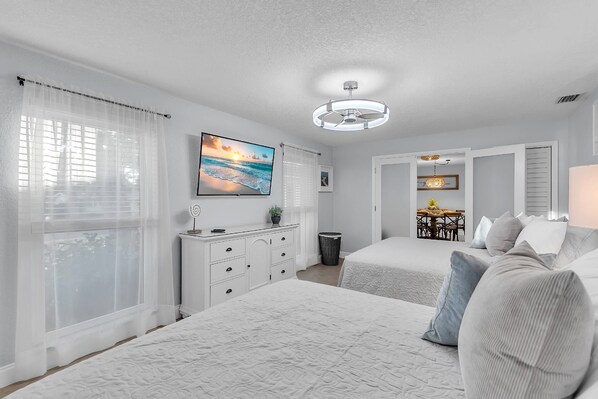 A bedroom with two beds, a dresser, a TV, and a ceiling fan.