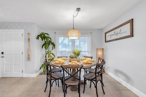 Un coin repas avec une table ronde, des chaises, un luminaire suspendu, une plante en pot et un mot encadré accroché au mur.