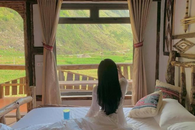 Una habitación con una cama, vistas a colinas verdes y una barandilla de madera en el exterior.