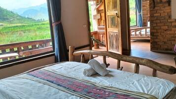Una cama con una colcha estampada, un cabecero de madera y vistas a un paisaje verde a través de una ventana.