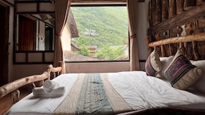 A traditional room with a bed, wooden headboard, and a view of a village through a window. - O'Chau Meo Vac Homestay Ha Giang (Pa Vi)