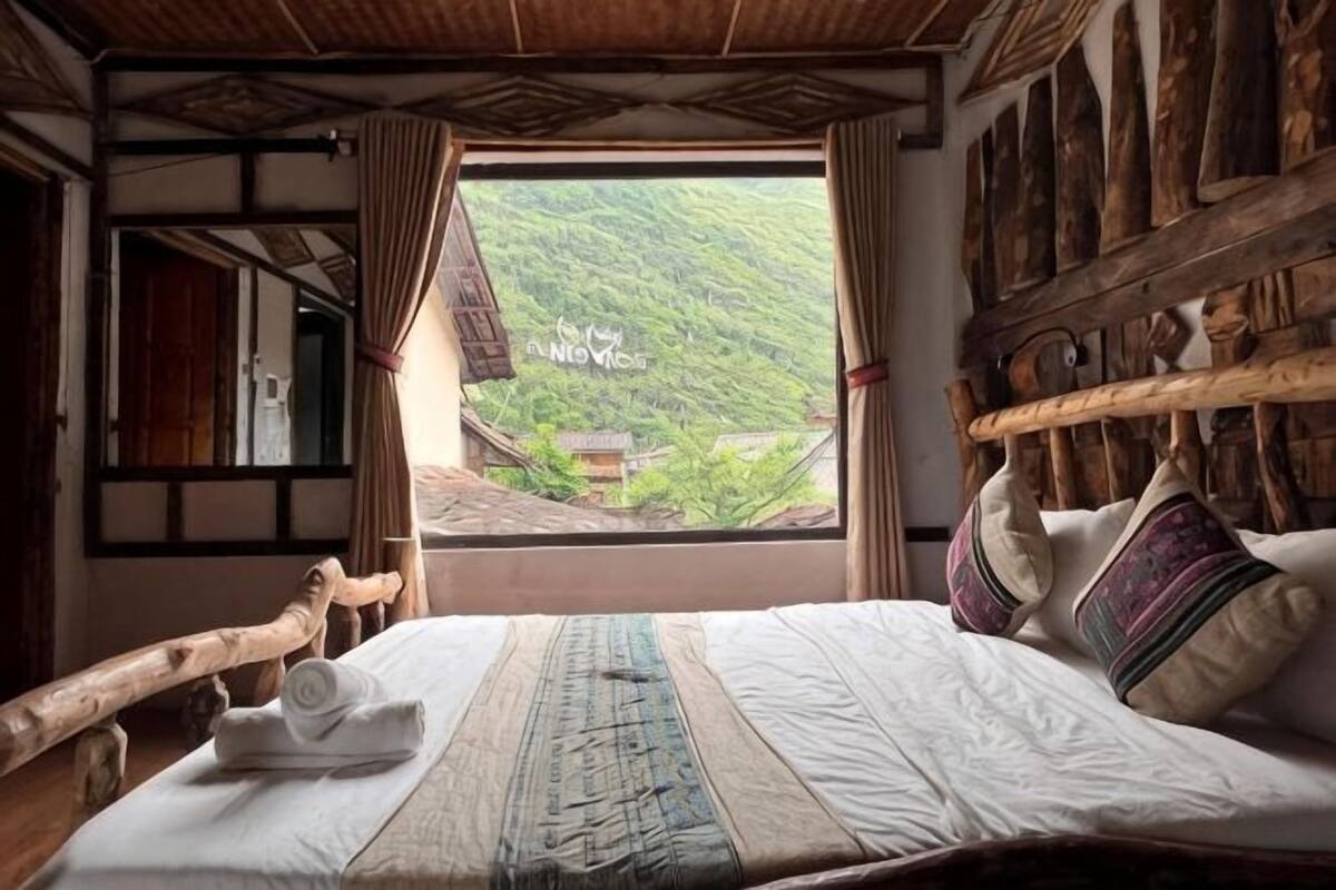 Ein traditionell eingerichteter Raum mit Bett, Holz-Kopfteil und Blick auf ein Dorf durch ein Fenster.