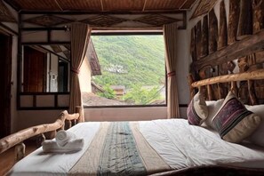 A traditional room with a bed, wooden headboard, and a view of a village through a window. - O'Chau Meo Vac Homestay Ha Giang (Pa Vi)