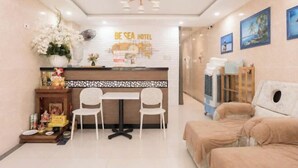 A hotel reception area with a counter, two chairs, a sofa, and a decorative wall. - Be Sea Hotel Da Nang (Da Nang)