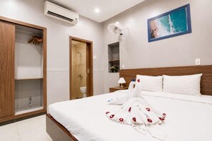 A hotel room with a bed, a wooden wardrobe, a shower, a fan, a painting, and a nightstand with a lamp. - Be Sea Hotel Da Nang (Da Nang)