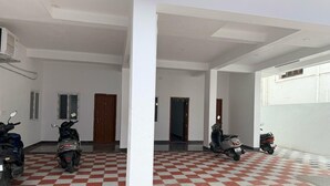 A covered parking area with a checkered floor, several parked scooters, and a corridor leading to a door. - Kavitha Stay Inn (Namakkal)