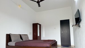 A bedroom with a bed, a wardrobe, a ceiling fan, a door, and a TV mounted on the wall. - Kavitha Stay Inn (Namakkal)