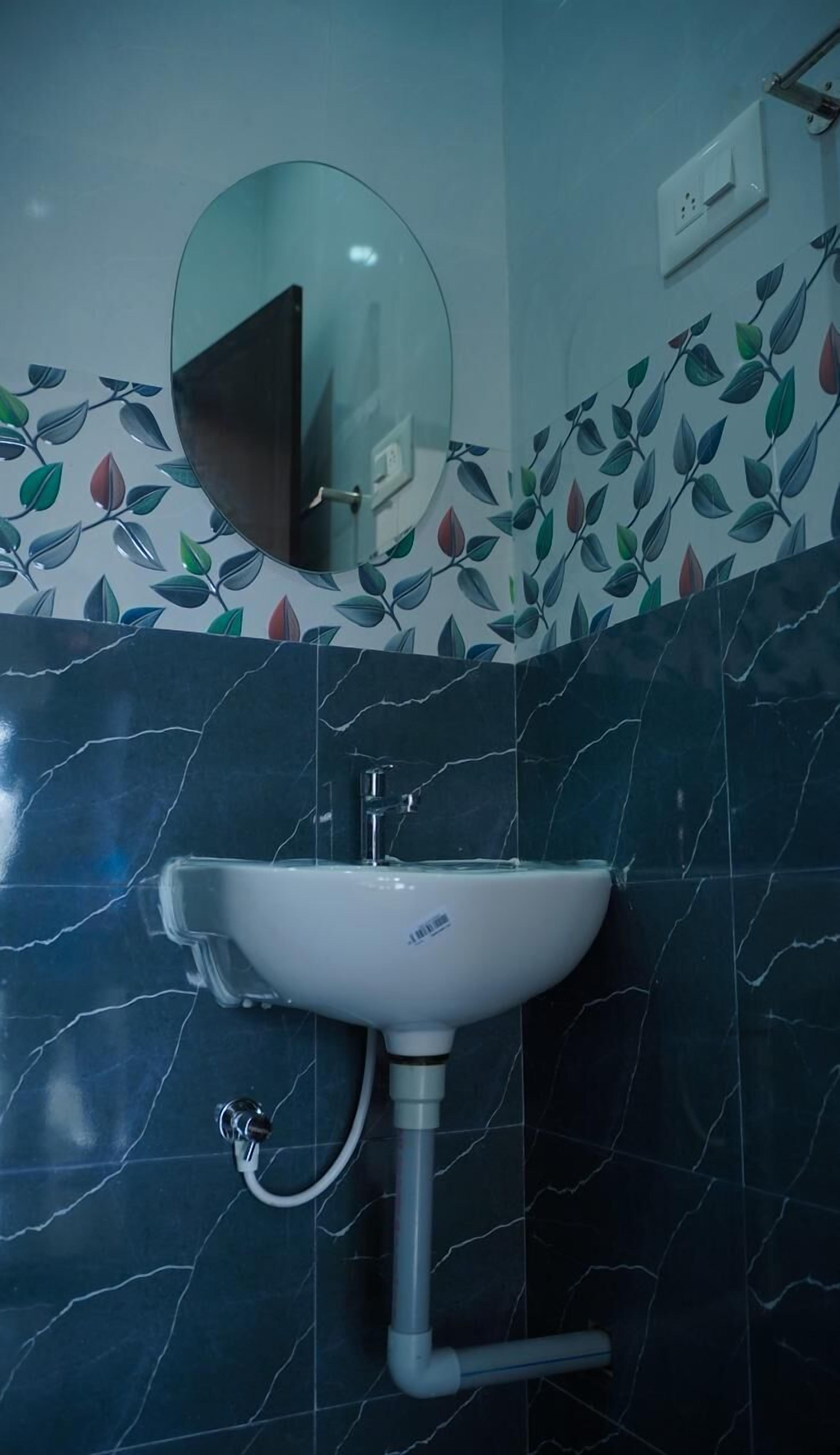 Un baño con un lavamanos blanco, un espejo y una pared con un diseño de hojas.