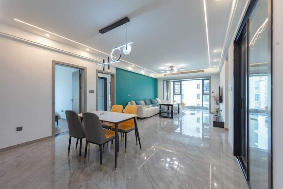 A modern interior with a dining area, a sofa set, and a large window providing natural light.