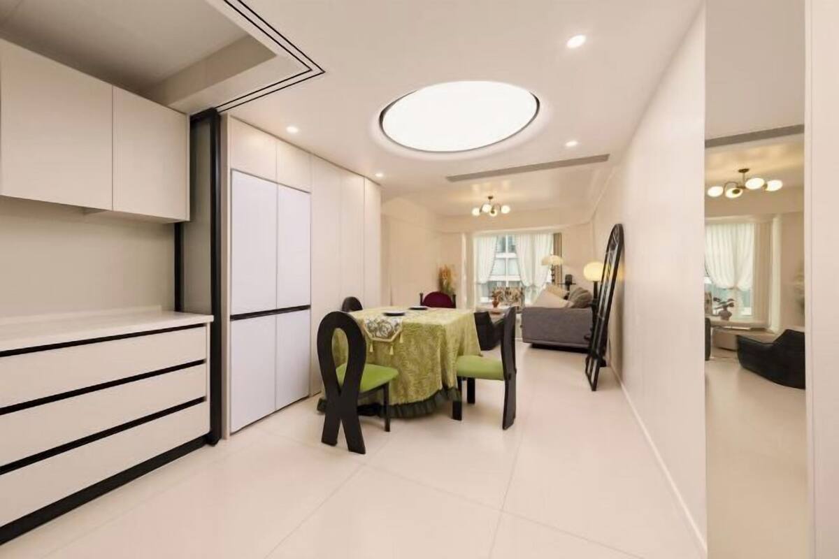 A modern kitchen with white cabinets, a dining area with a table and chairs, and a ceiling light fixture.