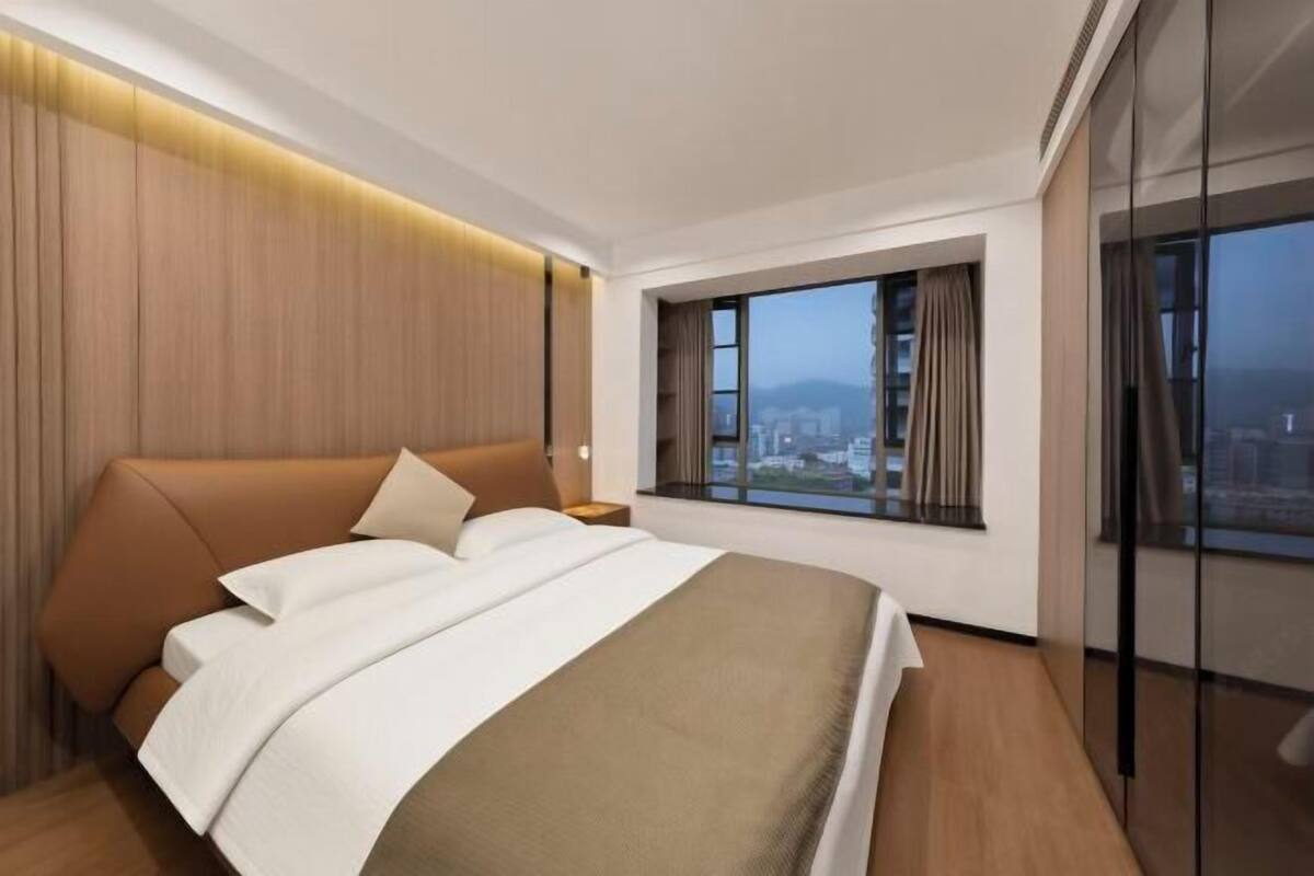 A modern hotel room with a large bed, a nightstand, a window with curtains, and a city view.