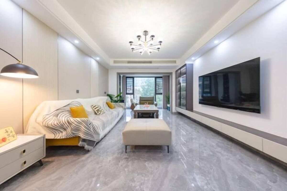 A modern living room with a sofa, ottoman, TV, and a ceiling light fixture.