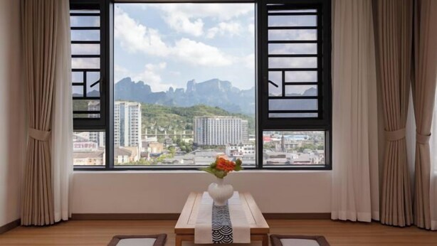A room with a large window, a table with a vase, and two cushions.