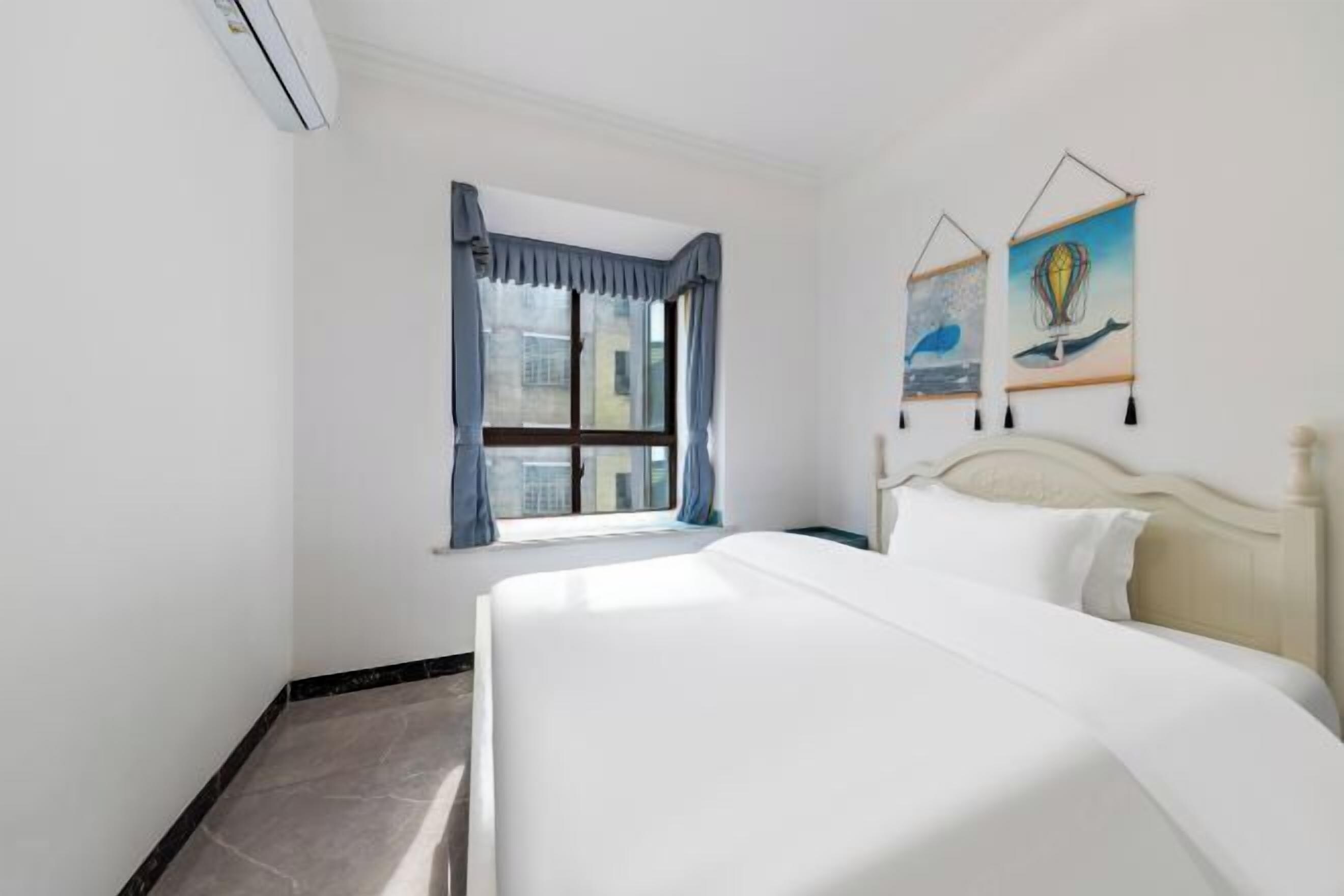 A hotel room with a bed, a window with curtains, and two wall-mounted artworks.