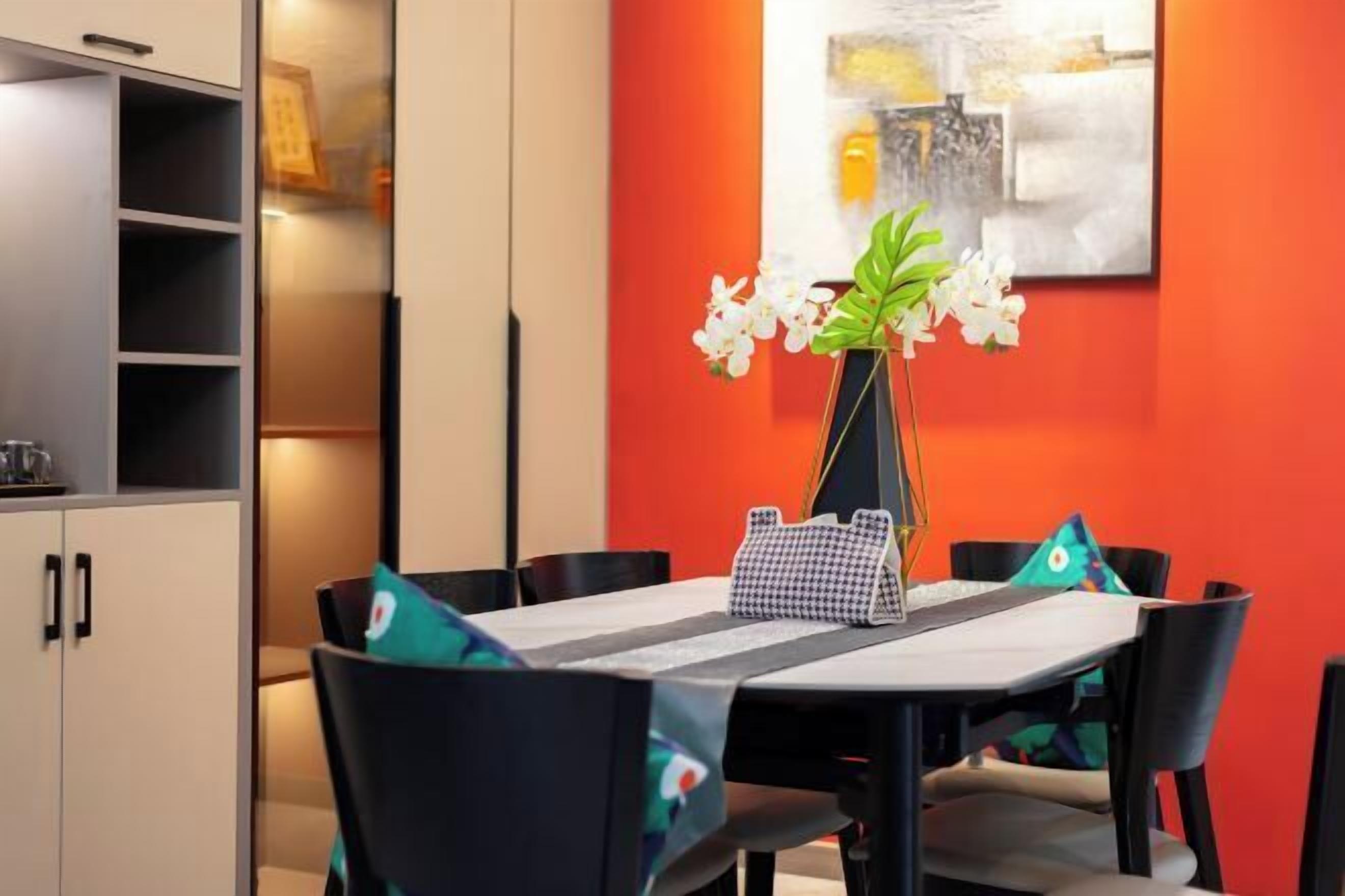 A dining area with a table set for four, surrounded by chairs, a vase with flowers, and a wall with a painting.