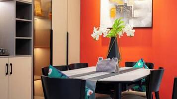 A dining area with a table set for four, surrounded by chairs, a vase with flowers, and a wall with a painting.