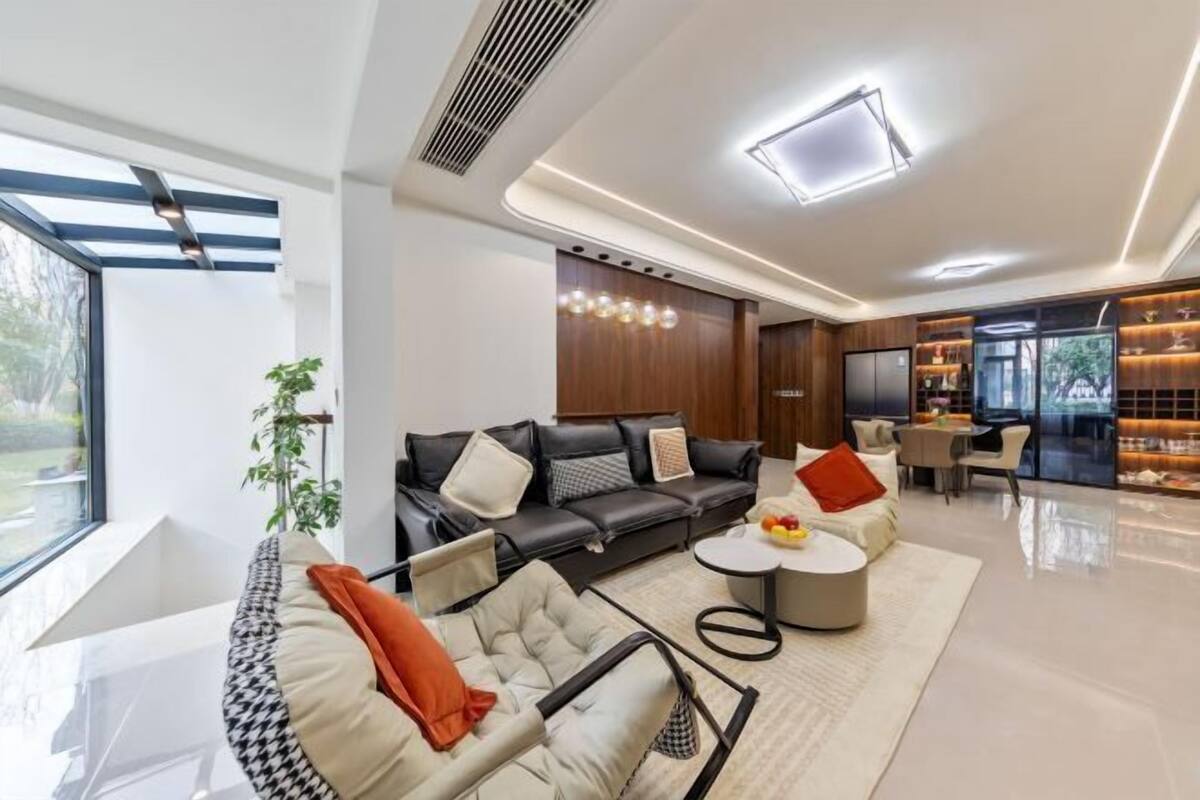 A modern living room with a sofa, armchair, and coffee table, a dining area with a table and chairs, and a kitchen with a counter and appliances.