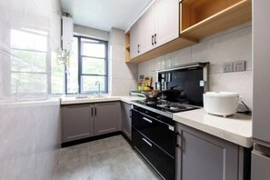 A modern kitchen with grey cabinets, a black stove, and a white countertop. - My Heart Returns · Zhangjiajie Zero-Pressure Luxury Dream Apartment (Zhangjiajie)