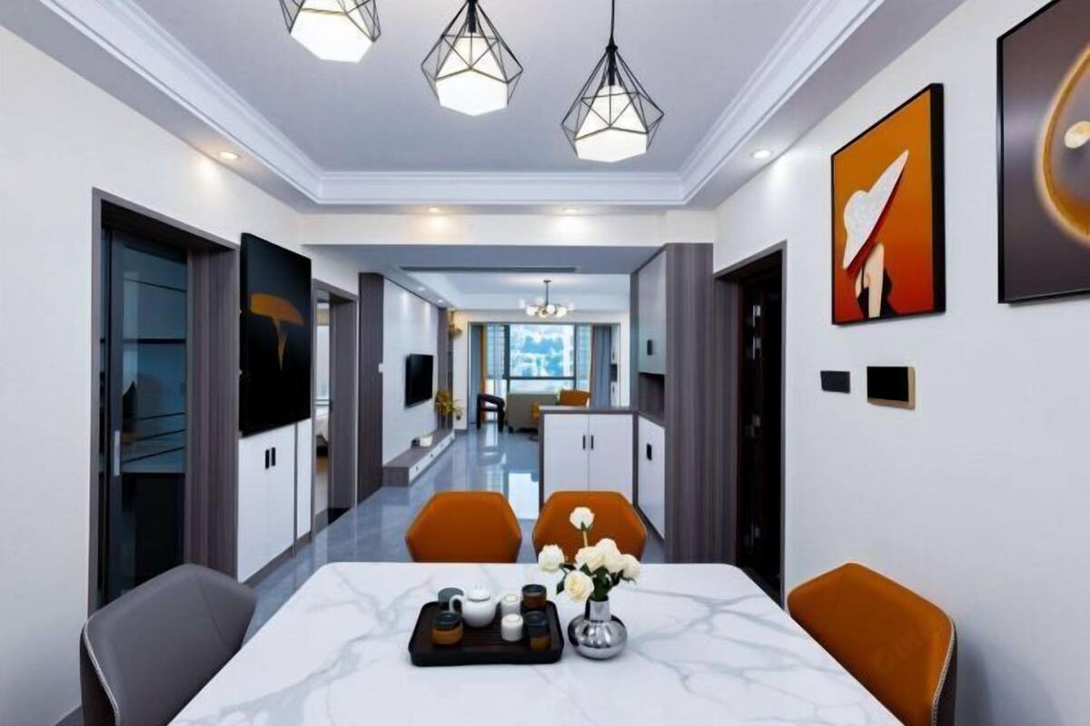 A modern hotel dining area with a marble table, orange chairs, and a chandelier.