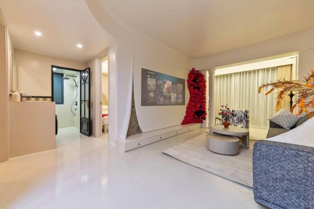 A modern living room with a white floor, a grey sofa, a red abstract sculpture, and a wall-mounted TV.