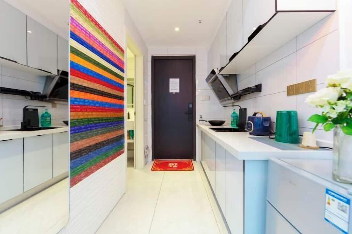 A modern kitchen with white cabinets, a colorful striped wall, and a red mat at the entrance.