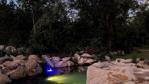 Een buiten zwembad omringd door rotsen, met een waterval en verlichte blauwe en gele lichten.