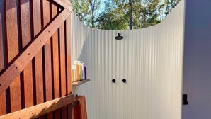 Een houten terras met een witte schutting, een klein grindpad en een plankje met toiletartikelen.