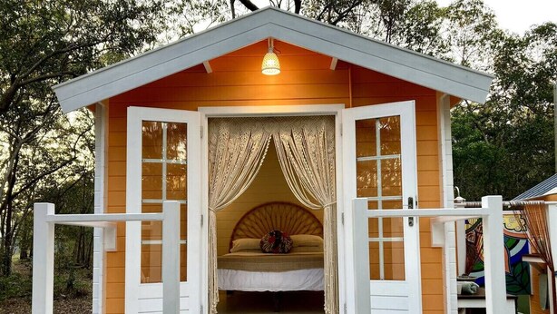 A cozy cabin with a bed, curtains, and a small porch. - Casa Naranja | Off-grid Hideaway Agnes Water 1770 (Captain Creek)