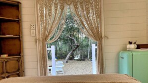 A bedroom with a bed, a window with curtains, a white chair outside, and a vintage green cabinet. - Casa Naranja | Off-grid Hideaway Agnes Water 1770 (Captain Creek)
