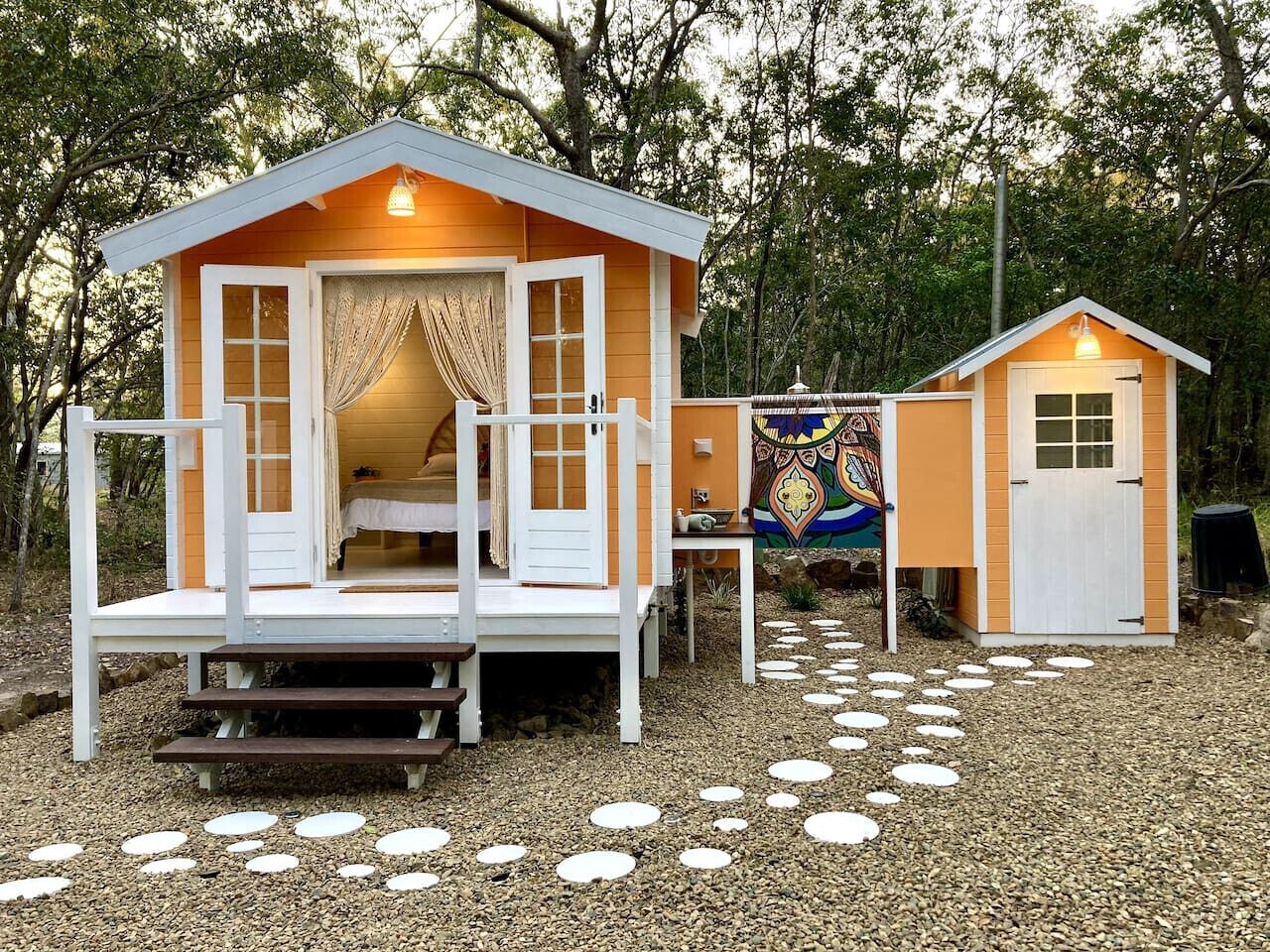 Une cabane avec une véranda, une petite terrasse et une fresque colorée en arrière-plan.