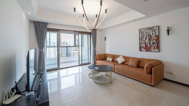 A modern living room with a leather sofa, a round coffee table, a flat-screen TV, and a large window offering a city view. - Tyms Xintiandi Elegant 3BR 2BA APT  (Shanghai)