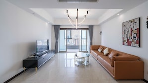 A modern living room with a sofa, a TV, a coffee table, and a large window with a city view. - Tyms Xintiandi Elegant 3BR 2BA APT  (Shanghai)