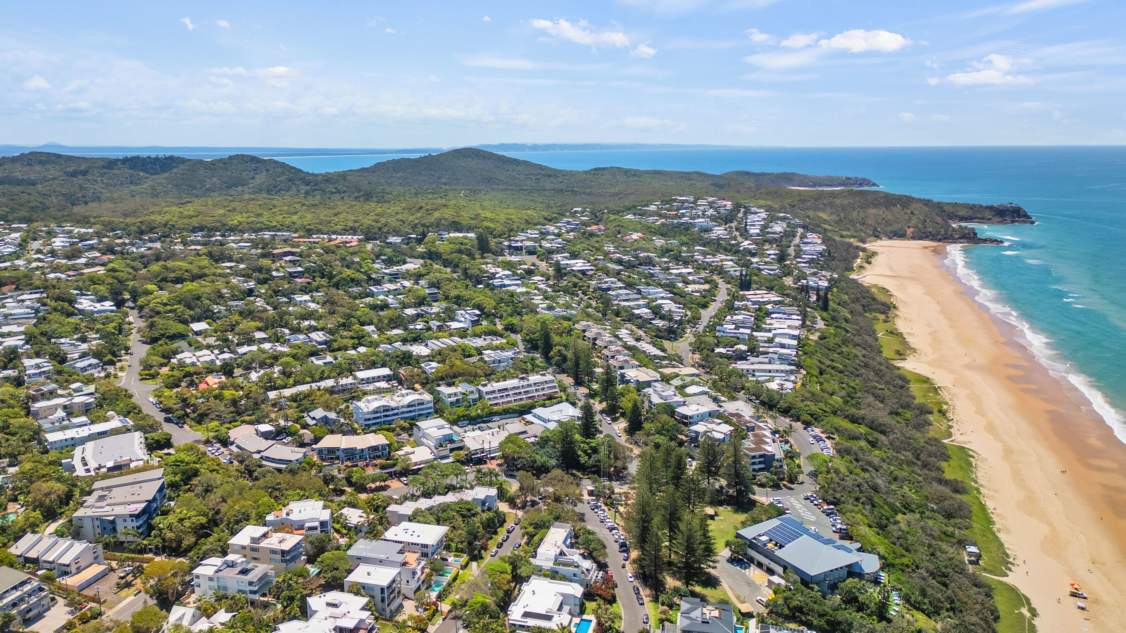 An aerial view of a coastal residential area with houses, roads, and a beach.