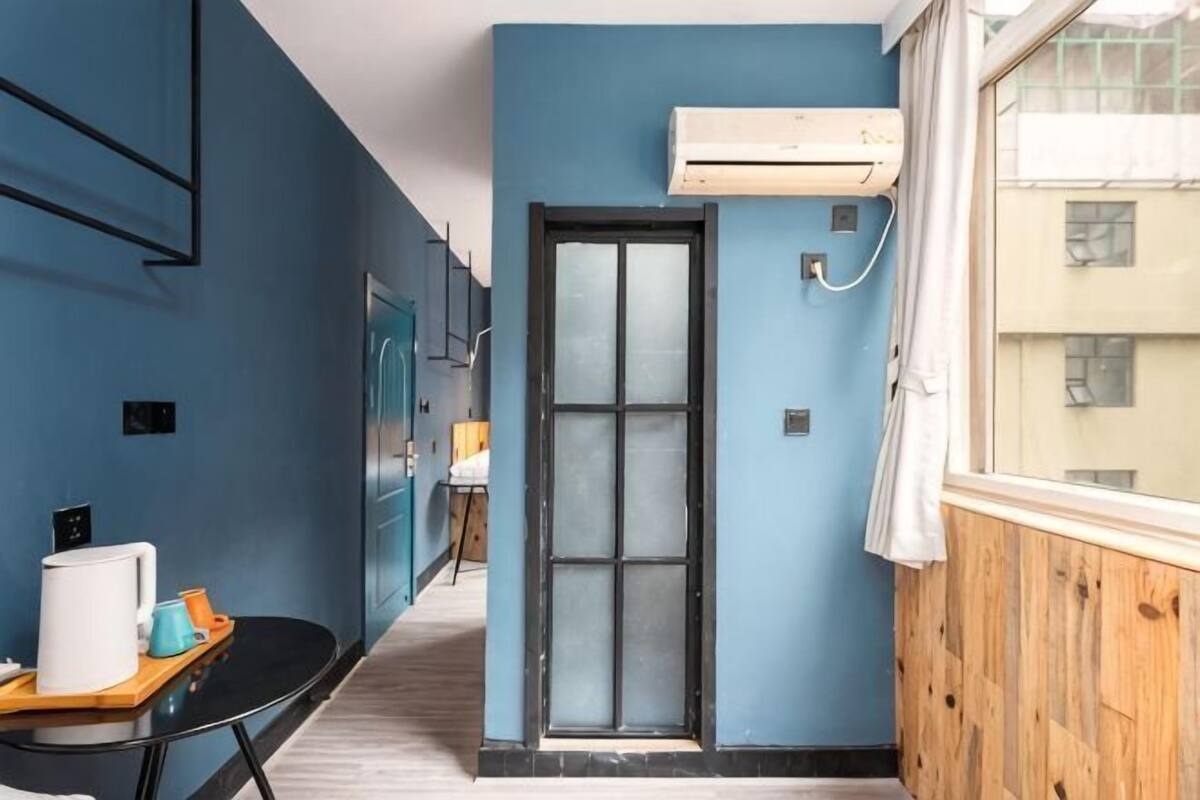 A narrow hallway with a blue wall, a wooden door, and a window with a view of buildings.