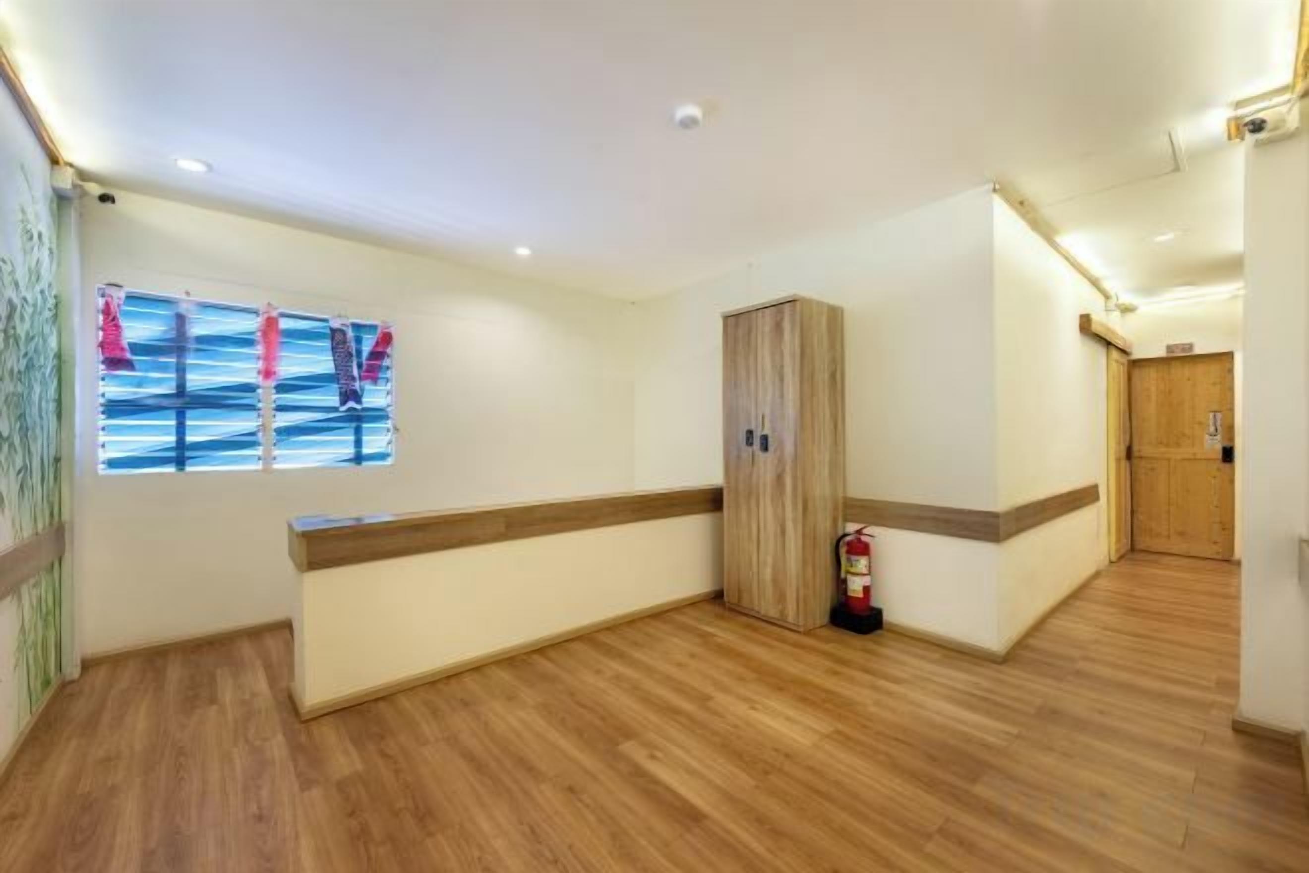 A hotel room with a wooden floor, a wooden wardrobe, a window with a view, and a fire extinguisher.