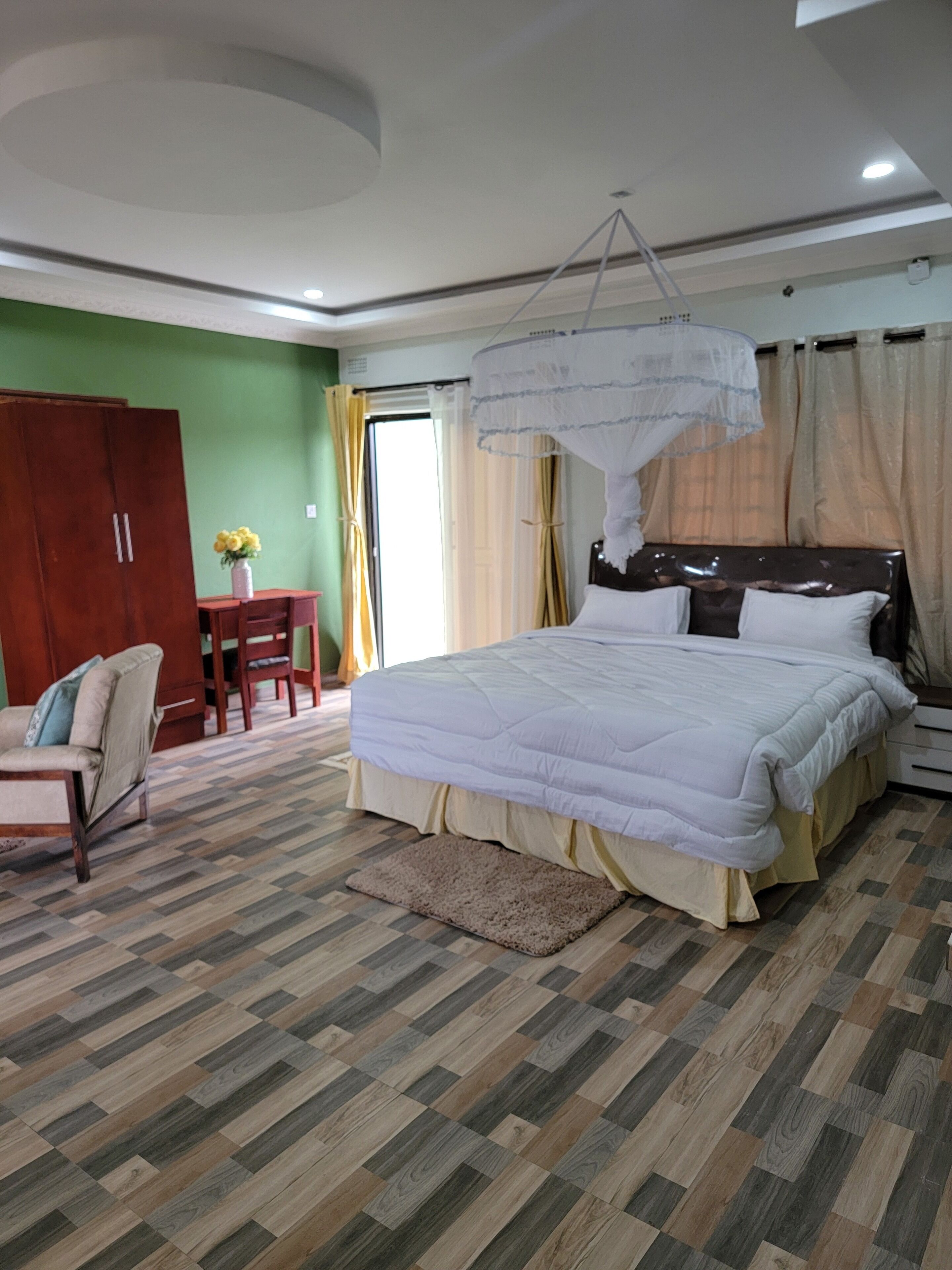 Un dormitorio con una cama grande, un armario de madera, un escritorio con silla y una ventana con cortinas.