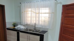 A kitchen with a sink, cabinets, and a window with sheer curtains. - Mew3 Apartments (Ndola)