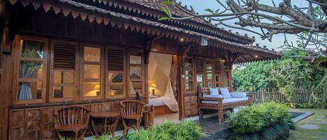 A traditional wooden house with a tiled roof, a bed with a canopy, and a seating area with chairs and a sofa.